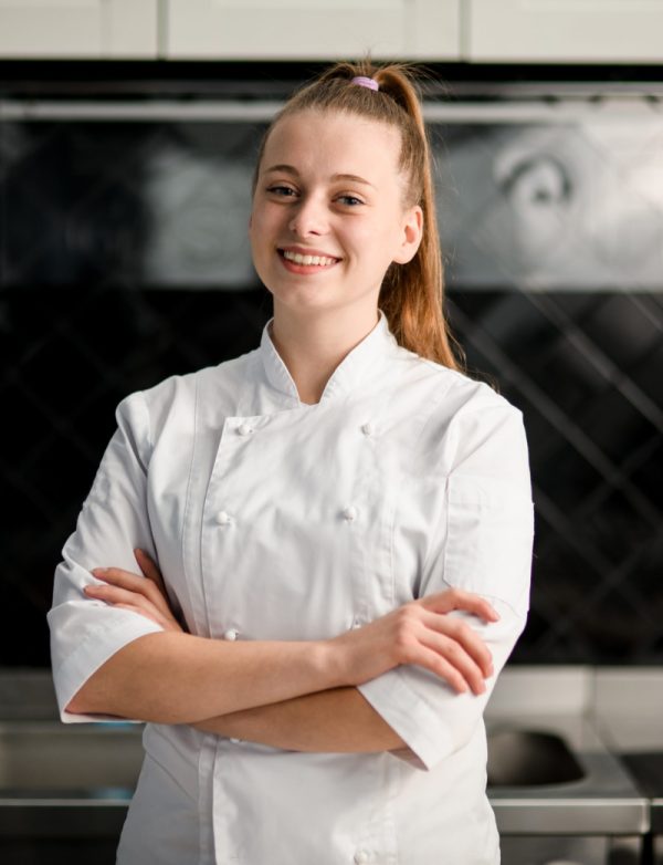 Young woman chef standing in a kitchen with her arms crossed