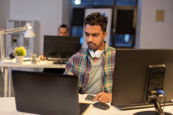 deadline, technology and people concept - creative man with laptop computer working at night office