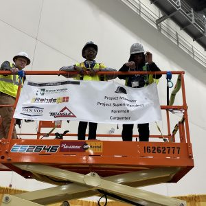 Students on a lift with a lift operator and an event sponsor sign.